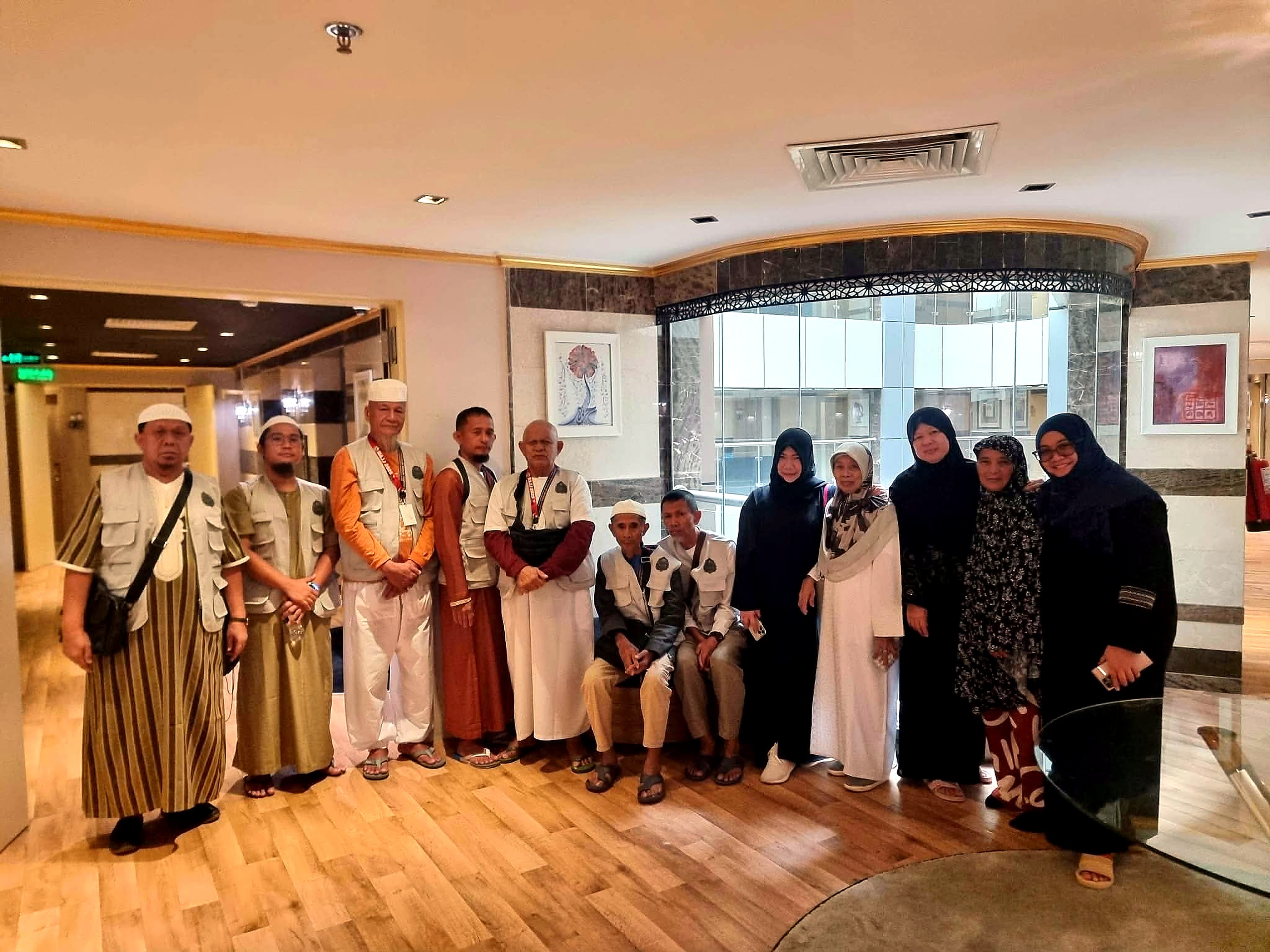 A group of men and women pilgrims, some wearing matching vests, gathered in a hotel hallway.